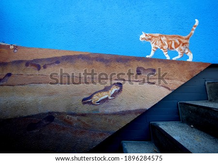 naturalistic painted red redhead cat walking over painted layers of earth with animals at a cellar staircase on the facade wall painting on a block of flats in Wuppertal, Germany