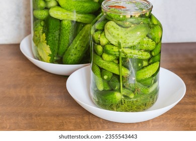 Naturally fermented quick pickled cucumbers in jar during souring against the other same jar on a kitchen table - Shutterstock ID 2355543443