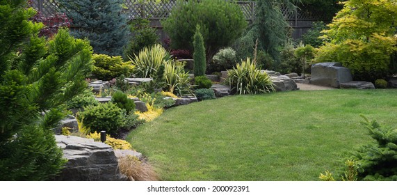 Naturally sculptured flat top rocks from northwest Oregon are placed in a beautifully landscaped backyard among a variety of perennial evergreens and shrubs. 