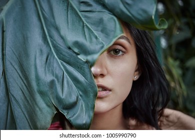 Nature, Beauty, Skincare And Organic Cosmetics Concept. Half Face Close Up Portrait Of Gorgeous Bob Haired Young Woman With Clean Skin Posing Outdoors, Hiding Herself Behind Large Fresh Green Leaf