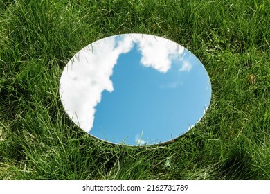 nature concept - blue sky and cloud reflection in round mirror on grass
