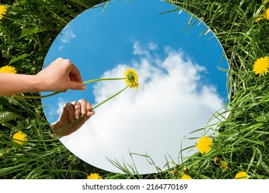 nature concept - hand with dandelion touching sky reflection in round mirror on summer field - Shutterstock ID 2164770169