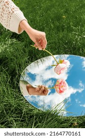 Nature Concept - Hand With Peony Flower And Sky Reflection In Round Mirror On Summer Field