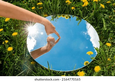 nature concept - hand touching sky reflection in round mirror on summer field - Shutterstock ID 2164770165