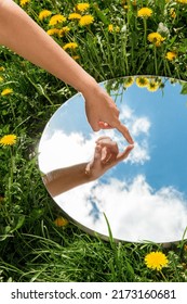 nature concept - hand touching sky reflection in round mirror on summer field - Shutterstock ID 2173160681