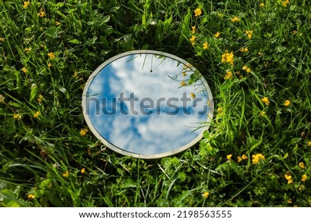 Nature concept - sky and clouds reflection in round mirror in the grass with flowers. Mirror lies on the summer field. Template