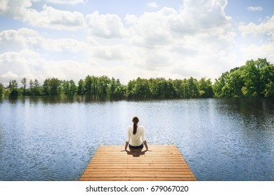 Nature getaway.  Woman sitting on a wooden dock next to lake.  - Powered by Shutterstock