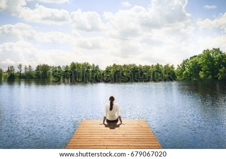 Nature getaway.  Woman sitting on a wooden dock next to lake. 