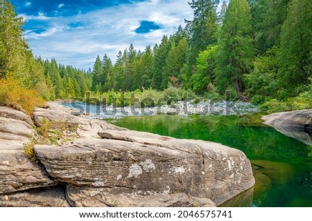Nature photograph of Nanaimo river with rock landscape green water blue sky and lush trees pebbles under water