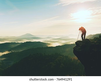 Nature photographer in the action.  Man silhouette above a misty clouds,  morning hilly landscape.