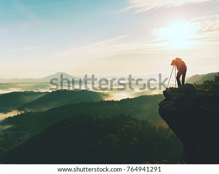 Nature photographer in the action.  Man silhouette above a misty clouds,  morning hilly landscape.
