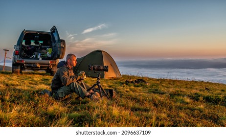 A nature photographer taking photos of mountain sunrise and eating breakfast. - Powered by Shutterstock