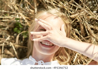 Nature, Summer Holidays, Vacation And People Concept - Close Up Of Happy Young Woman Lying On Cereal Field And Covering Face By Hand