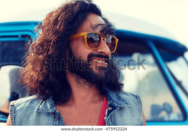 nature, summer, youth\
culture and people concept - smiling young hippie man in sunglasses\
over minivan car
