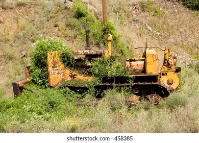 Nature wins - growing brush and weeds begin to cover an old bulldozer left abandoned near the North Platte River in Colorado - side view, vertical orientation.