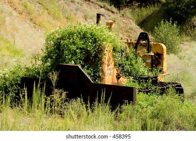 Nature wins - growing brush and weeds begin to cover an old bulldozer left abandoned near the North Platte River in Colorado - front view, horizontal orientation.