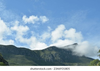 Nature's canvas: Rolling mountains adorned with billowing clouds, a serene symphony of earth and sky. Horizontal, blue sky.