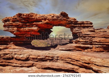 Nature's Window overlooking the Murchison River gorge in Kalbarri, Western Australia. Sunset light filters through a red sandstone rock arch, illuminating layered erosion and rugged desert landscape.