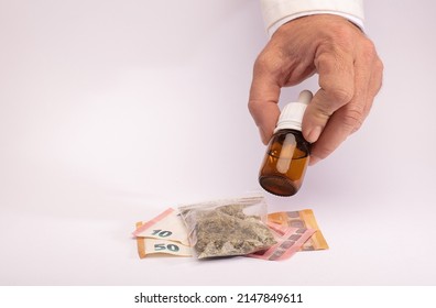 Naturist Dispensary Employee Presents Marijuana Oil In Dropper Dispenser, Cannabis Bag And Euros On A White Counter