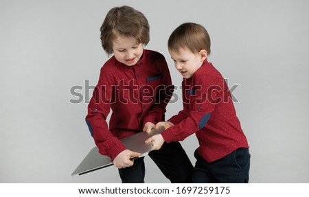 Naughty and active boys in isolation during quarantine. Two emotional brothers are trying to steal a laptop from each other for watching cartoons. Children are bored while at home. Cronovirus 