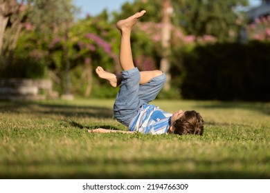 naughty boy is playing alone in the garden. lies on his back with his legs up. bored alone, don't know what to do - Powered by Shutterstock