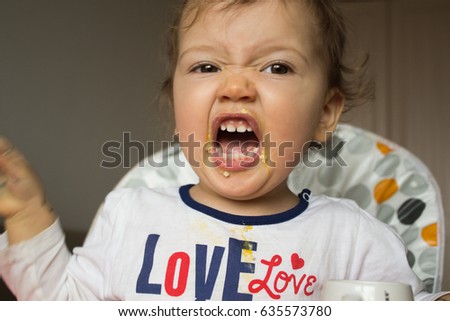 A naughty child does not want to eat. The kid is stained with porridge. Screaming child