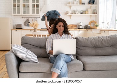 Naughty kid distract mother from work from home. Calm woman young mom typing on laptop computer sit on couch in living room with active small son fighting pillow. Motherhood and remote worker concept