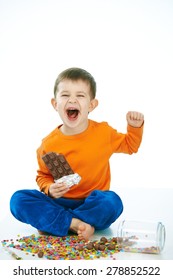 Naughty Little Kid Eating Chocolate Sitting Cross-legged On Floor, Sweets Spilt. Laughing, Hand In Hair, Isolated On White.