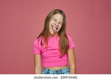 Naughty little positive child girl showing tongue, grimace, teasing, make faces, closed eyes on pink studio background - Powered by Shutterstock