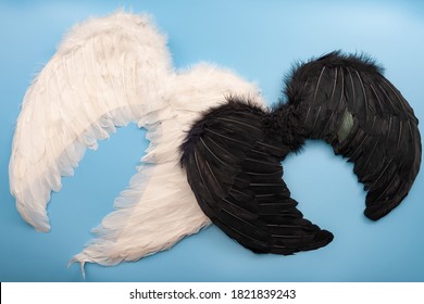 Naughty And Nice, Christian Mythology And The Struggle Between Good And Evil Concept With Photograph Of White Wings Representing An Angle And Black Wing For A Demon Isolated Of Blue Background