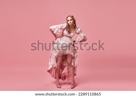 Naughty princess. Portrait of charming blond lady, queen wearing dress and standing with upset face on pink studio background. Concept of medieval, beauty, old-fashioned clothes, human emotions, ad