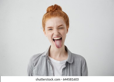 Naughty teenage girl with ginger hair and freckles misbehaving, sticking out her tongue at camera as a sign of disobedience, protest and disrespect. Human emotions, reactions, feelings and attitude