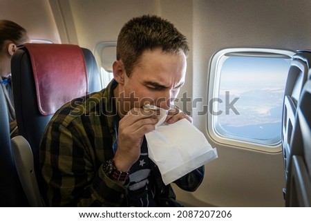 Nausea during the flight. A young guy gets carsick in transport. Nervous young man with aviophobia breathing into paper bag in airplane