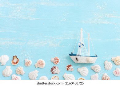 nautical concept with white sail boat and seashells over blue wooden background