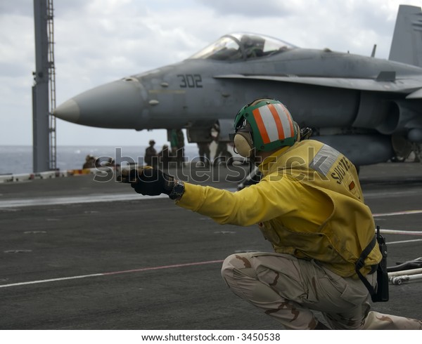 A Naval Officer signals for an F-18\
Hornet to launch on board an aircraft\
carrier