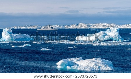 A naval ship navigating through icy waters with floating icebergs in the foreground and snow-covered mountains in the background under a clear sky.