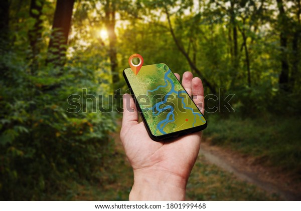 Navigation map with forest terrain and\
river on smartphone display. Concept of tourism and orienteering.\
Man hand hold in hand phone with use on-line maps\
