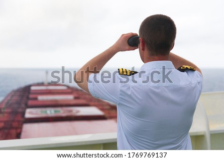 Navigator on the bridge of a large bulk carrier, doing lookout at the horizon with his binoculars

