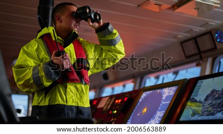 Navigator. pilot, captain as pat of ship crew performing daily duties with VHF radio, binoculars, logbook, standing nearby to ECDIS and radar station on board of modern ship 