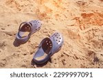 Navy blue crocs footwear on the beach, vacation background. Blue trendy croc beach shoes. Vacation concept. Travel vacation banner background.