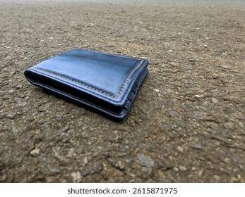 A navy blue leather wallet lies on the asphalt road. The image illustrates a lost personal item in a public outdoor environment.