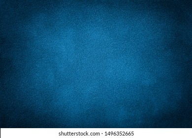 Navy blue matte background of suede fabric, closeup. Velvet texture of seamless turquoise leather. Felt material macro with dark vignette.