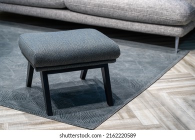 Navy blue stool next to fabric sofa in grey living room interior. Blue ottoman on a striped carpet - Shutterstock ID 2162220589