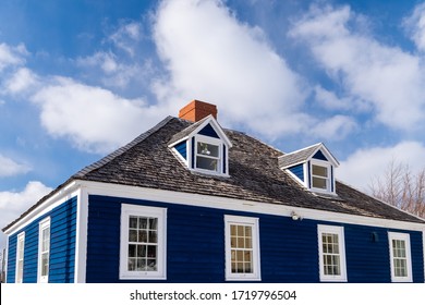 Navy blue vintage building with white trim and dark roof shingles. The top of the building has two dormers and multiple old double hung windows. The background has blue skies with white clouds.  - Powered by Shutterstock