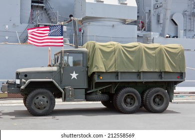 Navy Ship Sits In The Background Behind A Military Truck.