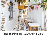 Naxos island, Cyclades Greece. Traditional outdoors cafe, wooden chair and table on cobblestone street. Whitewashed wall, plants around. Summer holiday destination.