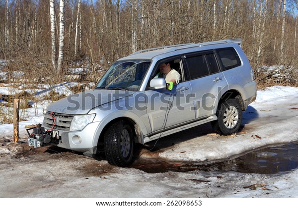 Nazia village, Leningrad Region, Russia - March 17,\
2015: Vehicle is stuck in the forest creek in an ice wood road, the\
driver uses a winch with remote control to pull the car out of the\
pit.