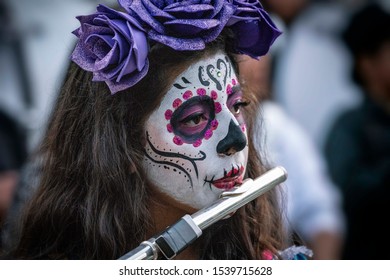 Nealtican / Mexico - November 5, 2018: A Young Woman With Face Paint And Makeup Plays The Flute In Celebration Of  Dia De Los Muertos Or Day Of The Dead In Mexico.