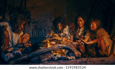 Neanderthal or Homo Sapiens Family Cooking Animal Meat over Bonfire and then Eating it. Tribe of Prehistoric Hunter-Gatherers Wearing Animal Skins Grilling and Eating Meat in Cave at Night Foto stock © 