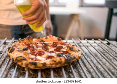 Neapolitan pizza style: close-up chef hand seasoning olive oil over chorizo sausage pizza on the pizza cooling rack on the kitchen counter before serving. Italian freshly baked Napoli pizza. - Powered by Shutterstock